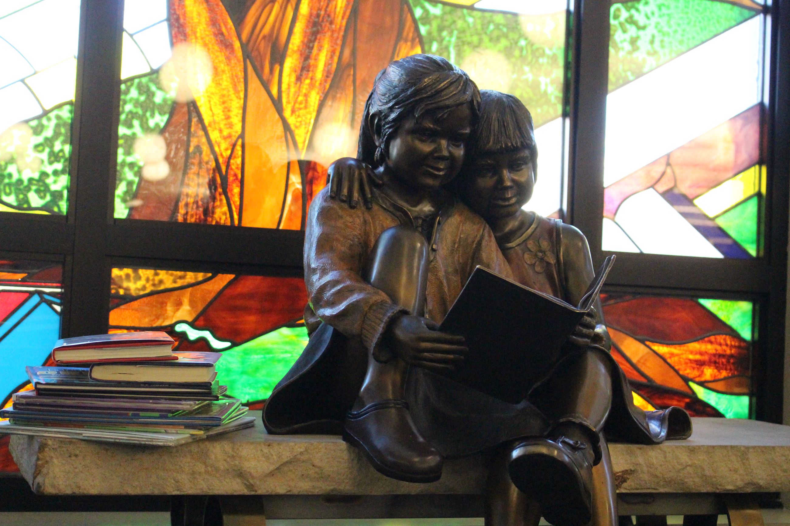 Bronze statue of little boy and girl reading a book while sitting on a bench