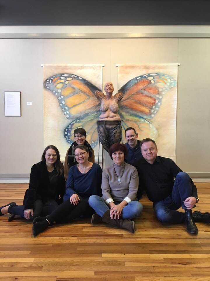 Six fine arts instructors from McPherson College pose in front of artwork in Friendship Hall